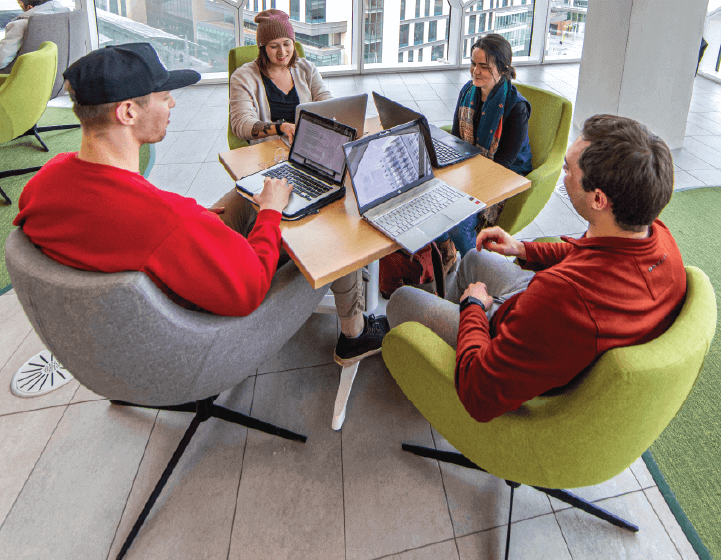background image: Four people sitting around a table working on their laptops. 