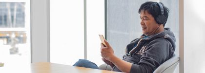 A adult sitting in a chair wearing headphones and watching something on his phone.