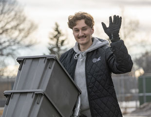 Man pushing grey bins waving his hand.
