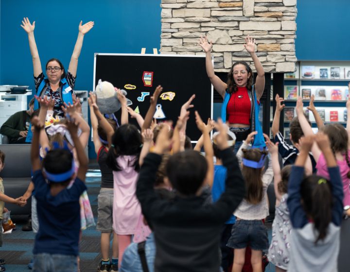 background image: A group of children participating in an activity with two Calgary Public Library staff.
