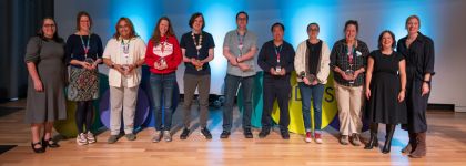 11 people standing on a stage. Eight people are holding awards.