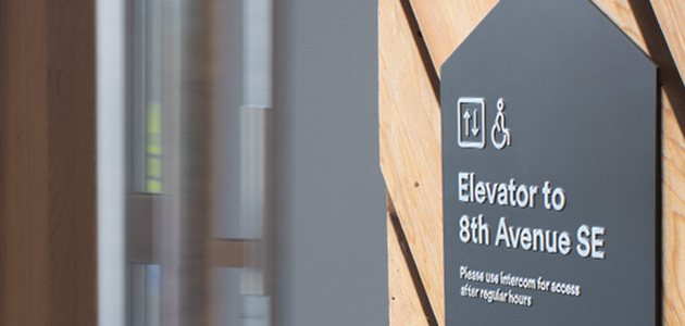 A panel on a wall with an elevator and wheelchair icon and the words Elevator to 8th Avenue SE