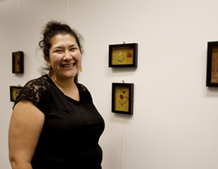 A photograph of an artist standing in front of their artwork and smiling at the camera. 