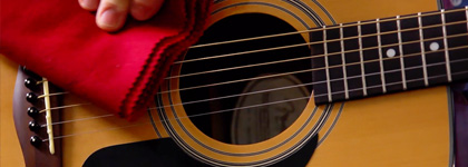 A visual of someone cleaning an acoustic guitar with a red cloth.