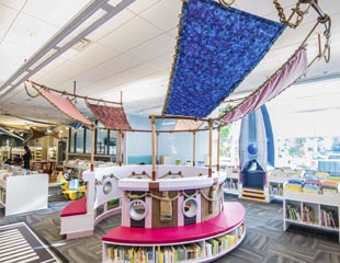 A cololurful and playful children's reading area designed like a ship, with fabric sails and book-lined walls. 