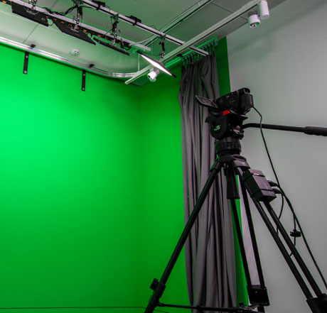 background image: A photograph of the audio video post-production studio. There is a camera in the shot as well as a green screen. 
