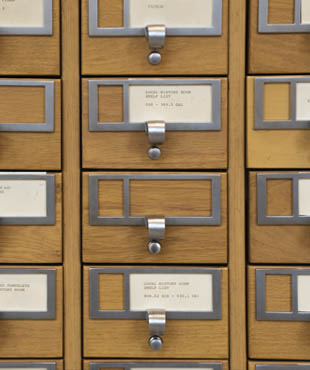 Close-up view of a traditional library card catalogue with wooden drawers and metal label holders.