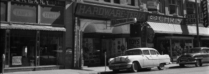 A vintage black and white photo of a hardware store on a city street in the 1950s.