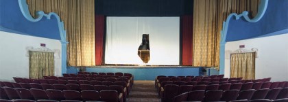 A view of the stage and seating area inside a vintage movie theatre, with red curtains, blue walls, and a blank movie screen.