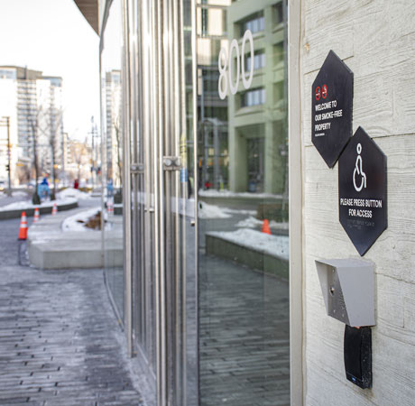 A visual of the outside entrance at Central Library. On the wall is signage that says "Welcome to a smoke-free property" and "Please press button for access." 