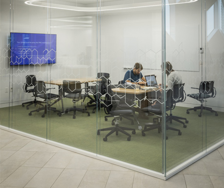 A visual of a meeting room. There are two people working on a computer inside.