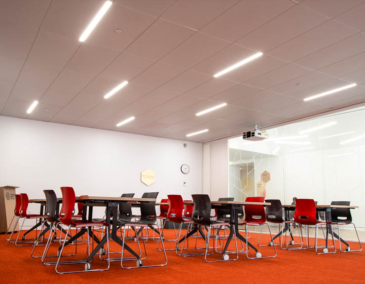 background image: This is a picture of a bookable meeting room on Level 0. In the picture, there are many tables and chairs set up, and in the background, you can see the glass with a hexagon pattern etched in it.