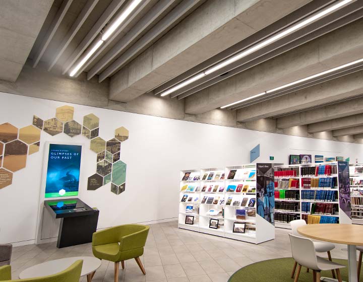 background image: A photography of Calgary's Story. On the left hand side there is a display that says "Glimpses of Our Past" with different images in a hexagon format above it. On the right side is a row of bookshelves with Calgary's  Story written on the side of them.