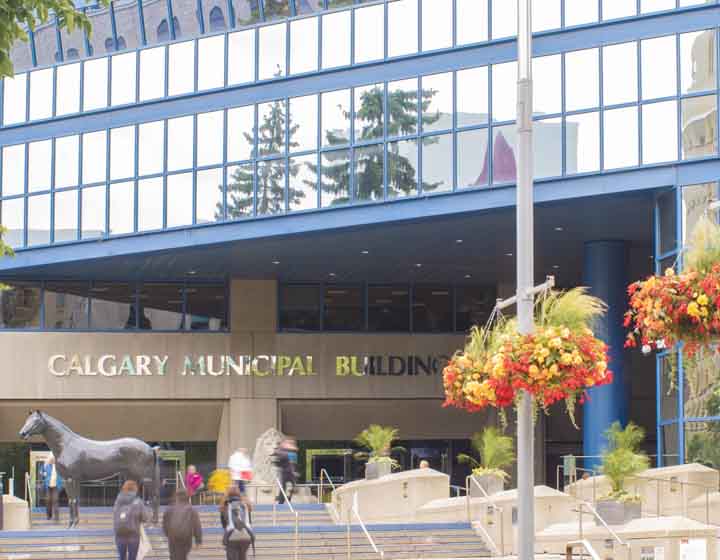 background image: A photo of the Calgary Municipal Building, which is next to Historic City Hall. The statue of the horse is visible in the image, as is the statue of the lion at the entrance of the building. 