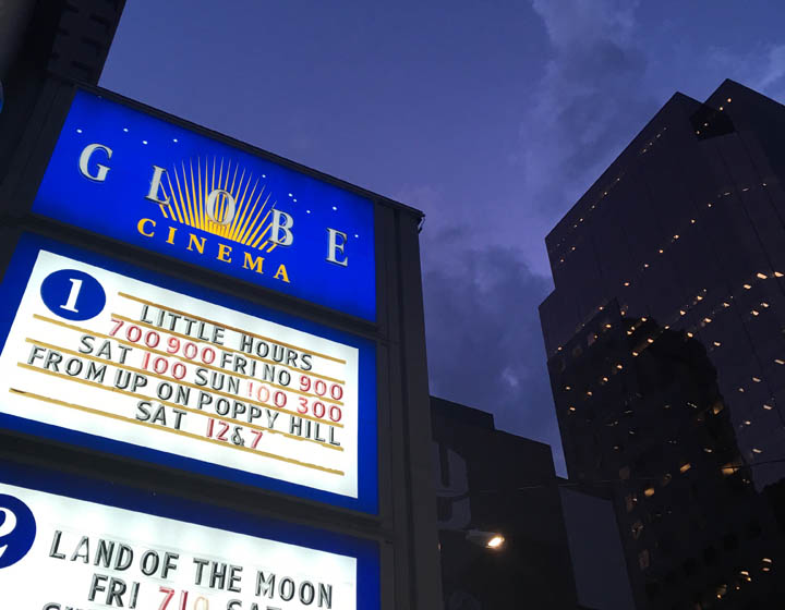 background image: This is a photograph of the "Globe Cinema" at night. It is a picture of the sign, and underneath it showcases film times for that evening. 