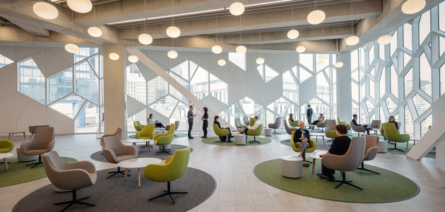 This is a picture of a bustling spaces compiled of tables and chairs with a visual of the hexagon windows in the background at Central Library.