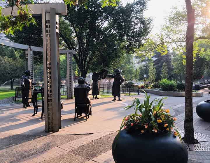 background image: A photo of Olympic Plaza. In the photo, the Famous Five statues and the wading pool in the background in the summer are visible.