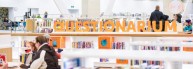 This is a visual of bookshelves with the word "Questionarium" in orange letters on top. Sitting below, a family is playing a game at the table.