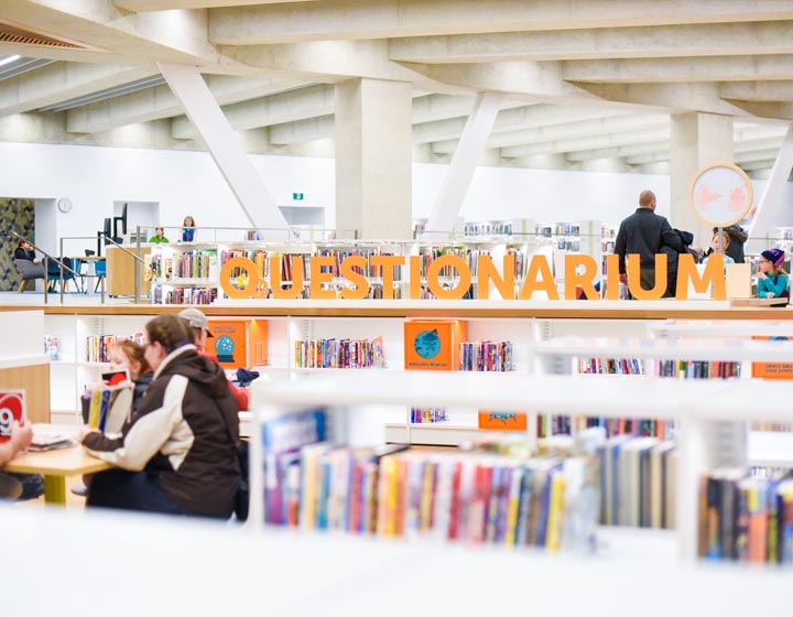 background image: This is a visual of bookshelves with the word "Questionarium" in orange letters on top. Sitting below, a family is playing a game at the table.