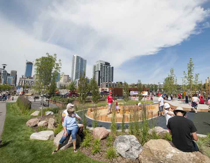 background image: A photograph of St. Patrick's Island. The photo shows rows of rocks at the front with people sitting on them. In the background, you can see little kids playing and see a visual of downtown Calgary.
