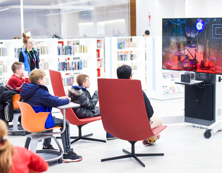 background image: A photograph of four teens sitting in red chairs, looking at a screen and playing a video game.