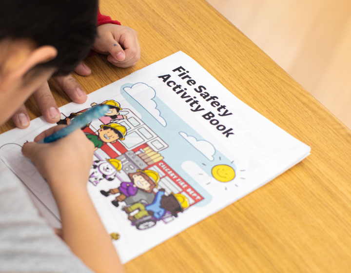 A photo of a child holding a pen and drawing on a booklet that says "Fire Safety Activity Book."