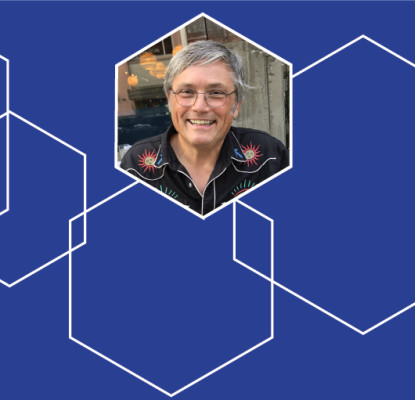 Photograph of 2026 Creative: AI Collaborative Artist in Residence Paul Freeman surrounded with blue and white hexagon graphics