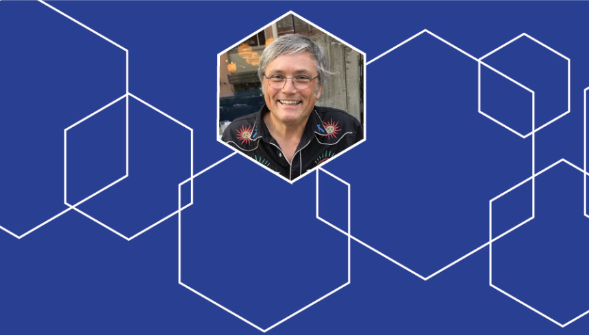 Photograph of 2026 Creative: AI Collaborative Artist in Residence Paul Freeman surrounded with blue and white hexagon graphics