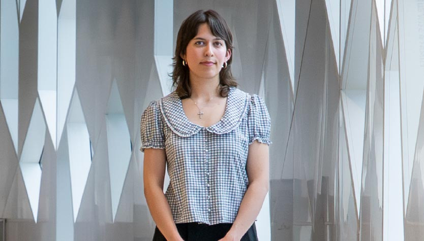 A person stands beside tall geometric windows inside Central Library. The person is the 2026 Historian in Residence. 