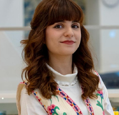Photo of Maedeh Mosaverzadeh, 2026 Newcomer Artist in Residence, inside a Library near an exhibit display and bookshelves. 