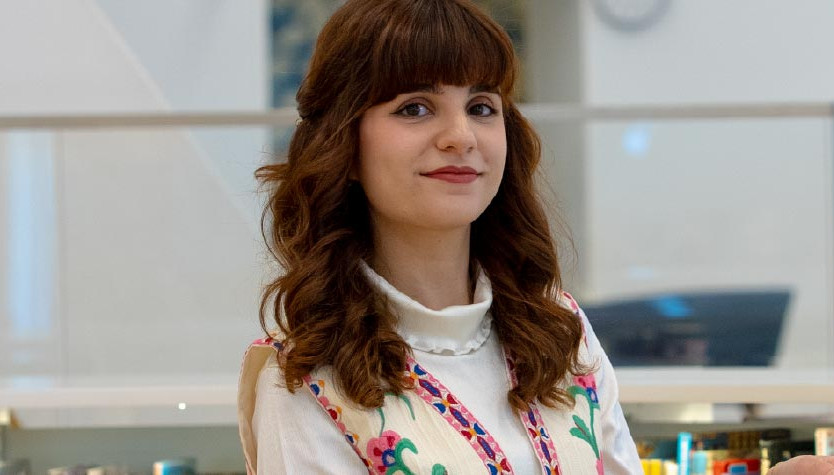Photo of Maedeh Mosaverzadeh, 2026 Newcomer Artist in Residence, inside a Library near an exhibit display and bookshelves. 
