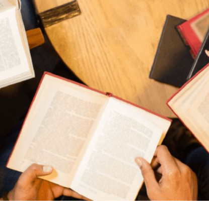 Photograph of three people sitting together at a table with their books open. 