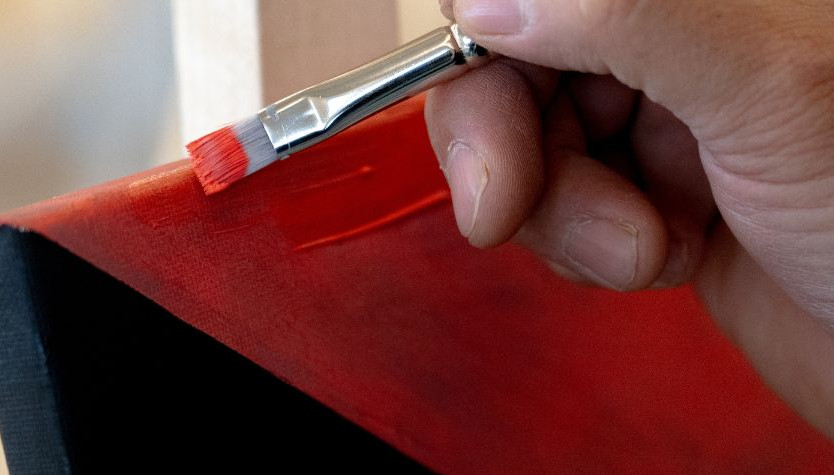 Indigenous Artist in Residence Darren Weaselchild's hands painting a read and black painting
