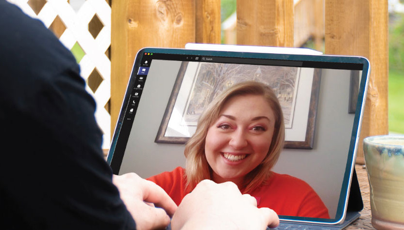 A person engaged in a virtual meeting on a laptop while sitting on a deck outside.