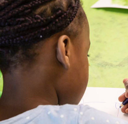 Photograph of a young person holding a pencil and writing on a piece of paper. 