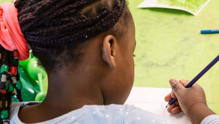 Photograph of a young person holding a pencil and writing on a piece of paper. 