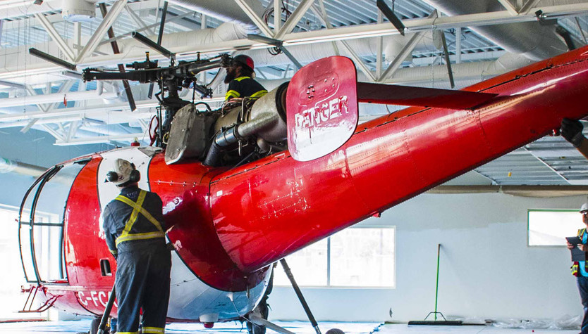 Photograph of a two individuals working on a red helicopter.