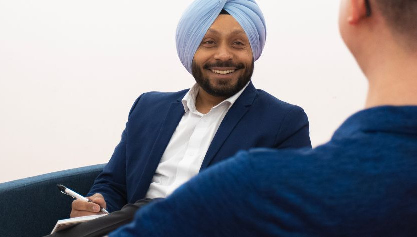 Two men speaking. One is smiling and writing in a notebook.