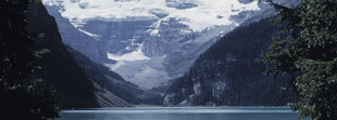 A photography of a mountain. In front of it is a lake, and you can see a canoe floating on the lake. 