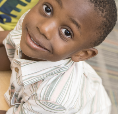 A young smiling boy holding an electronic reading device sitting at a table.