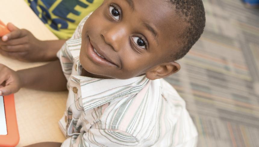 A young smiling boy holding an electronic reading device sitting at a table.