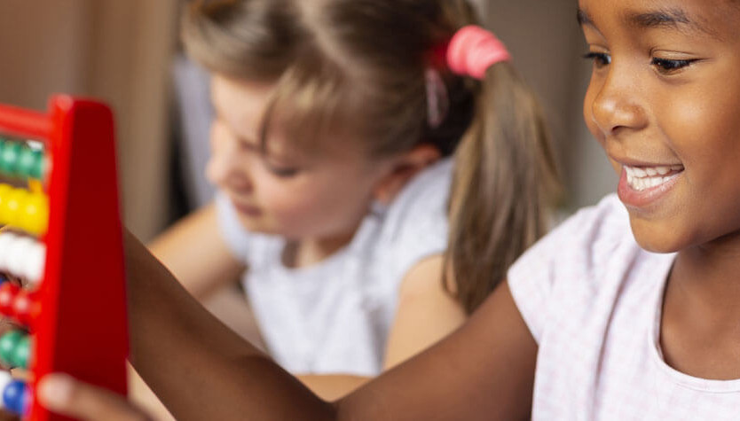 Two children engaged in math related activities. One child is using an abacus. 