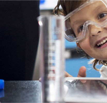 A child dressed up as a scientist in a lab coat looking at science lab equipment.