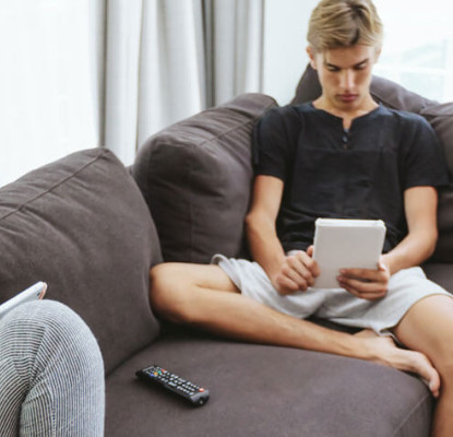 Photograph of two teenagers sitting on a couch each looking at a tablet.