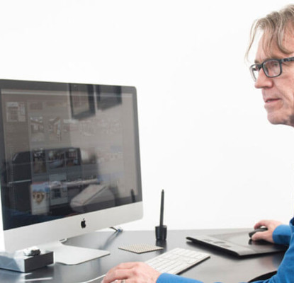 Photograph of a person wearing a blue shirt sitting in front of a desktop compute in a home office setting. 