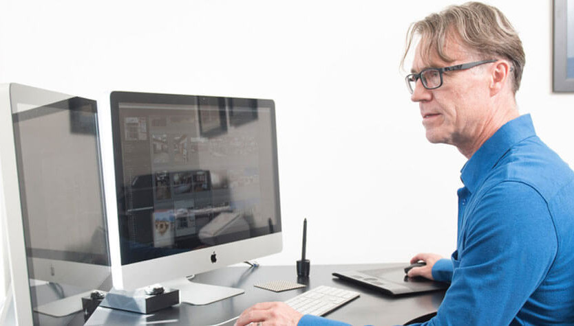 Photograph of a person wearing a blue shirt sitting in front of a desktop compute in a home office setting. 