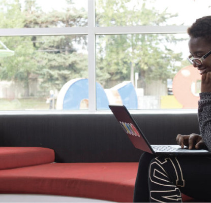 Individual sitting by a window using a laptop. 