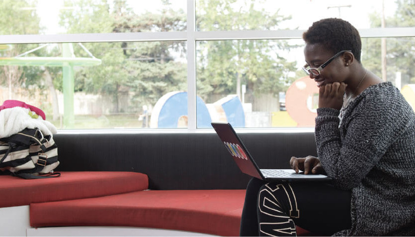 Individual sitting by a window using a laptop. 