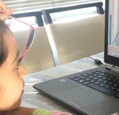 Photograph of a child sitting in front of a laptop screen. They are watching an online storytime program