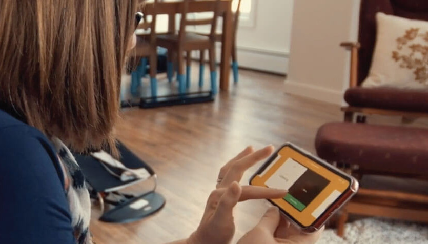 Photograph of an individual sitting in a home setting. They are using a smartphone application. 